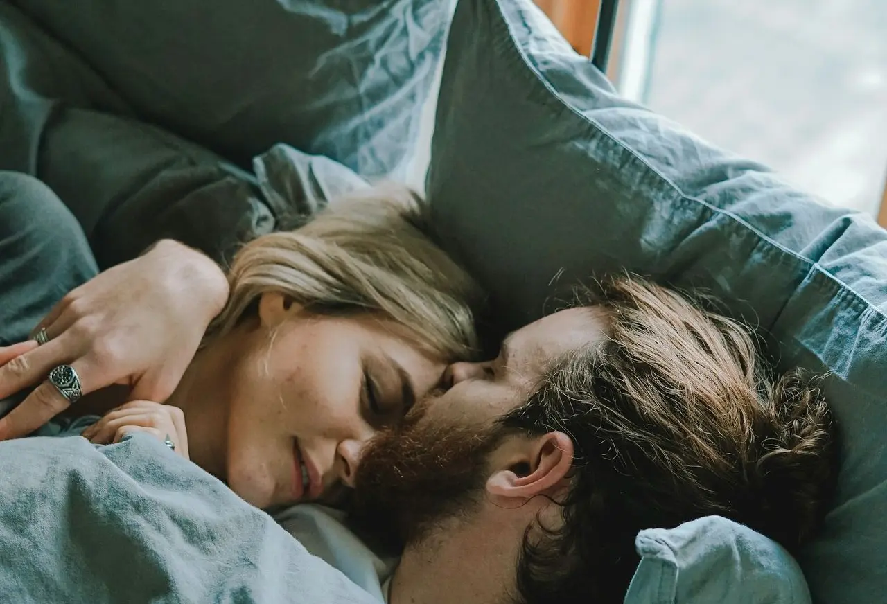 man kissing woman's forehead while lying on bed